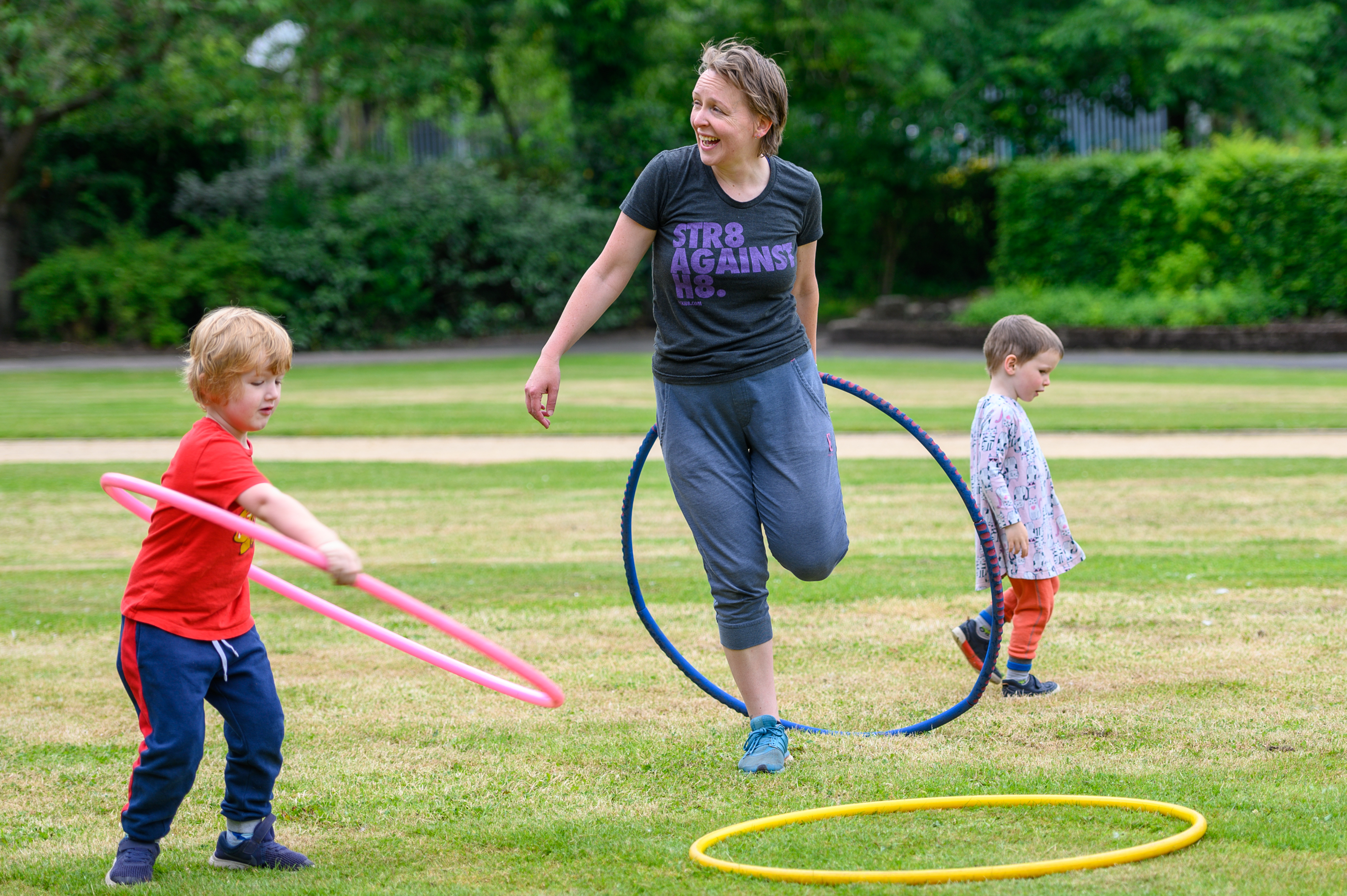 Mother laughing with hula hoop and children playing around her