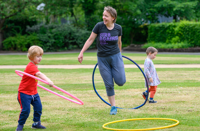 Mother laughing with hula hoop and children playing around her