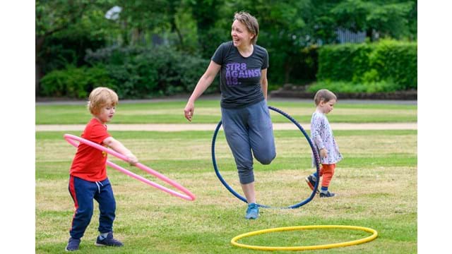 Mother laughing with hula hoop and children playing around her