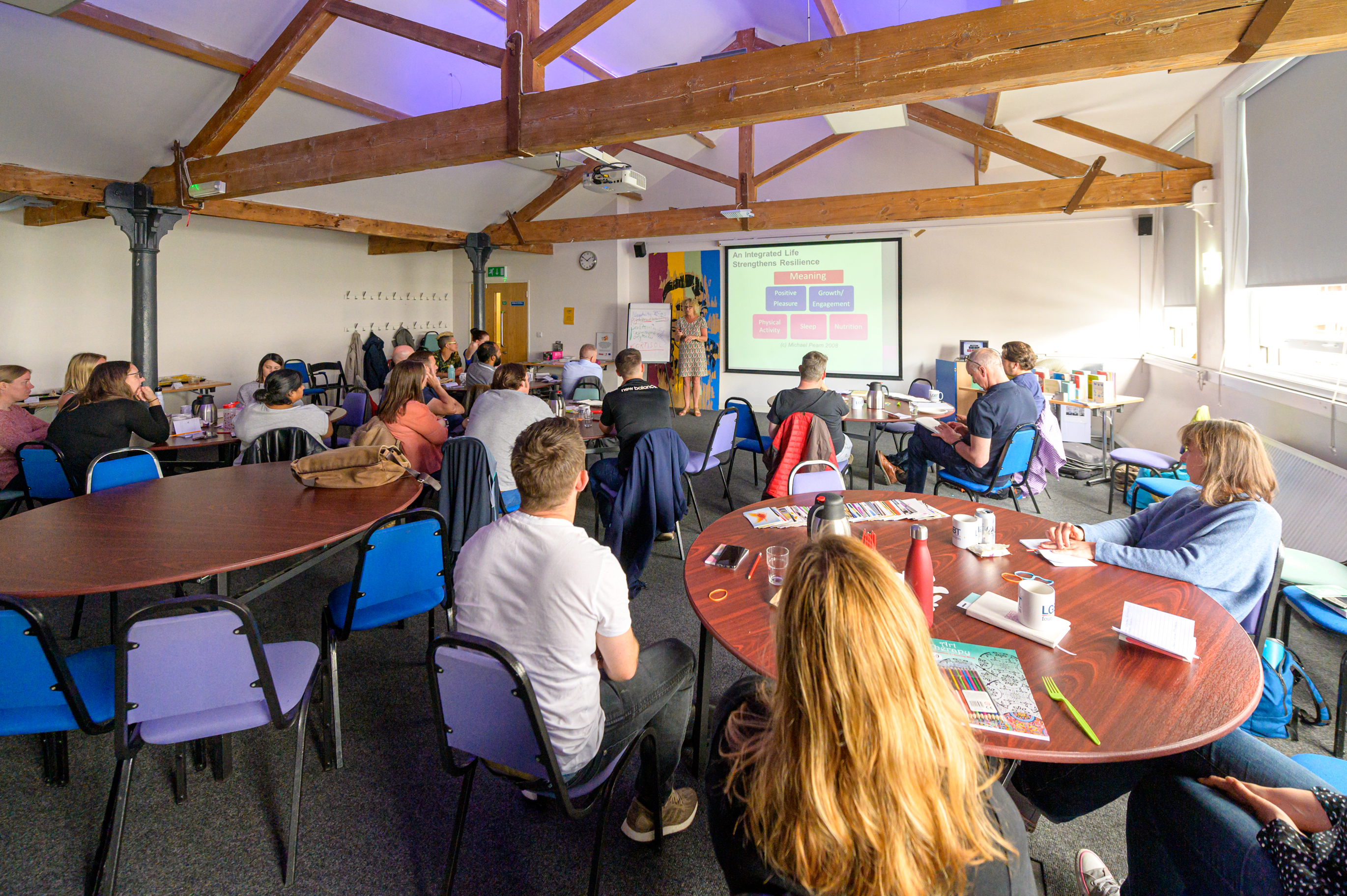 Groups of people sat around tables with a presenter in front of a screen