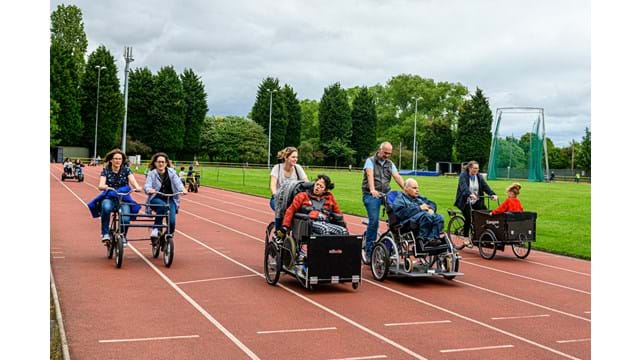 Many people on various types of bike cycling around an athletics track