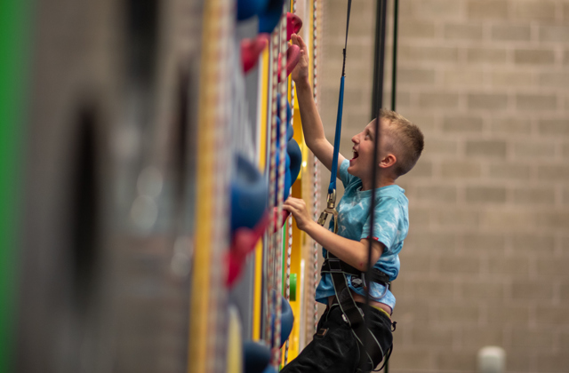 Young boy excitedly climbing up an indoor climbing wall