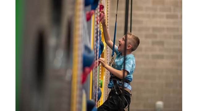 Young boy excitedly climbing up an indoor climbing wall