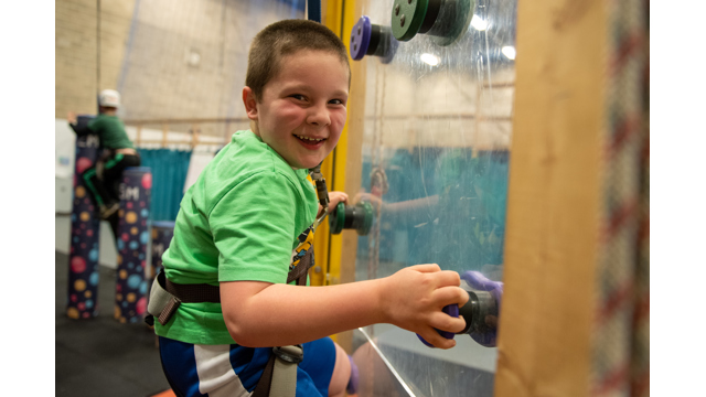 Young boy climbing up an indoor climbing wall smiling at the camera