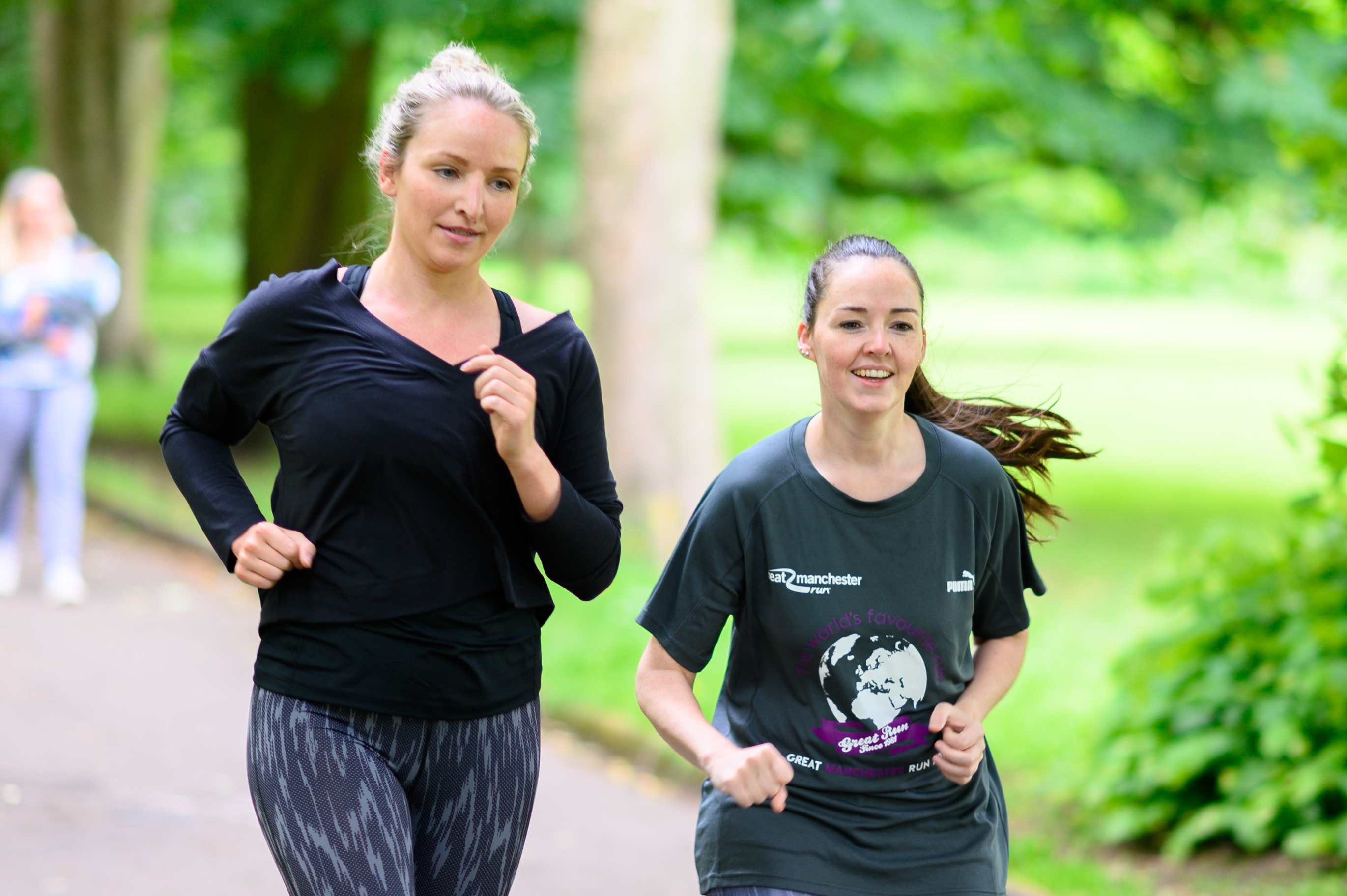 Two women jogging through the park, smiling