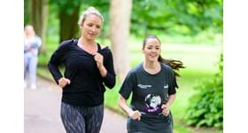 Two women jogging through the park, smiling