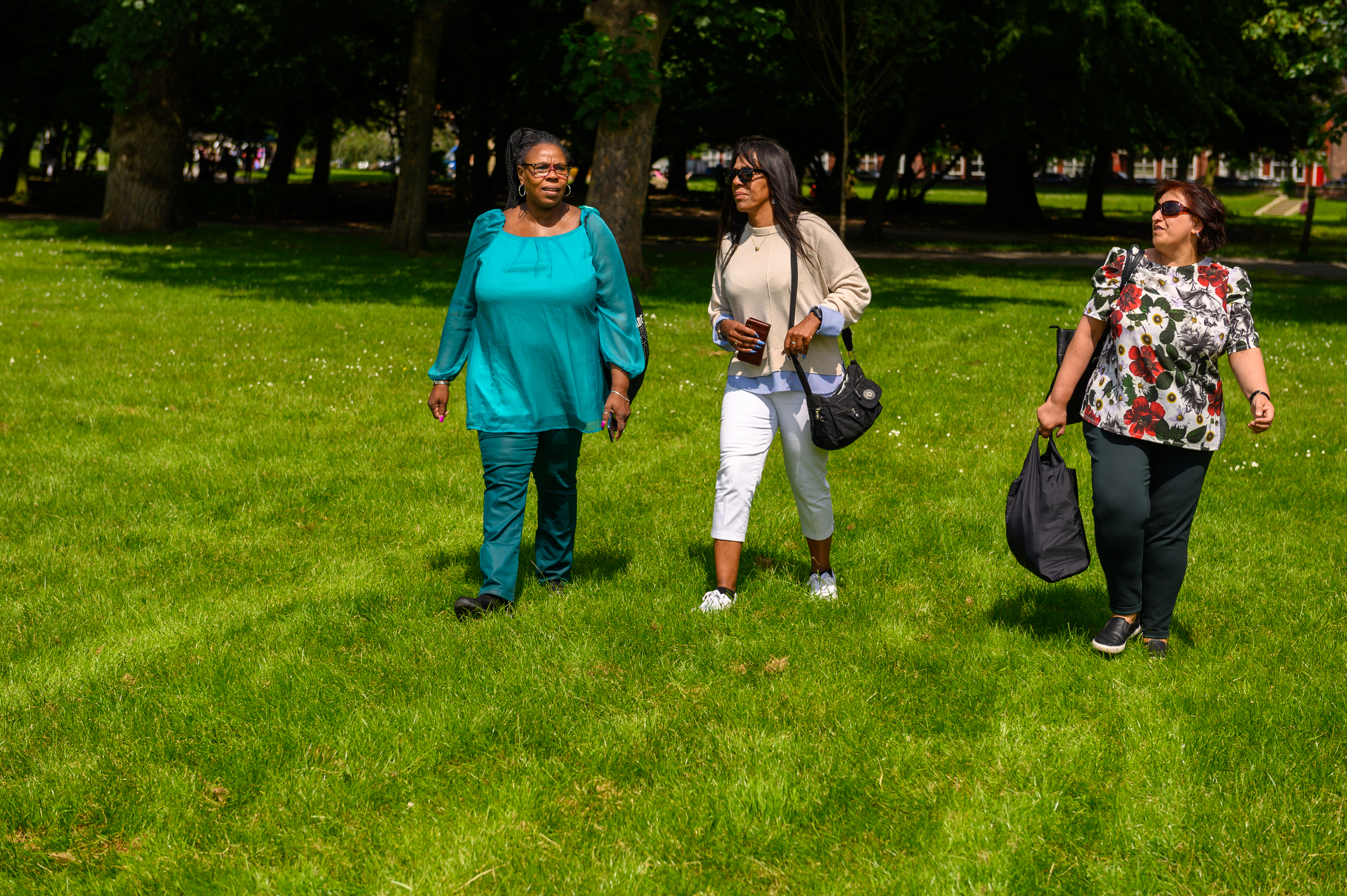 Three women walking across the grass in a park