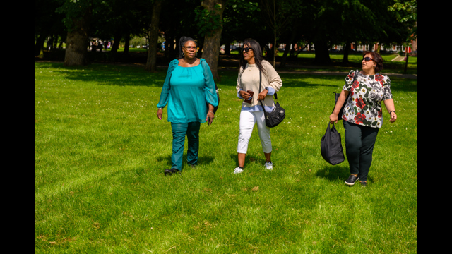 Three women walking across the grass in a park