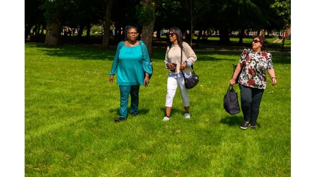 Three women walking across the grass in a park