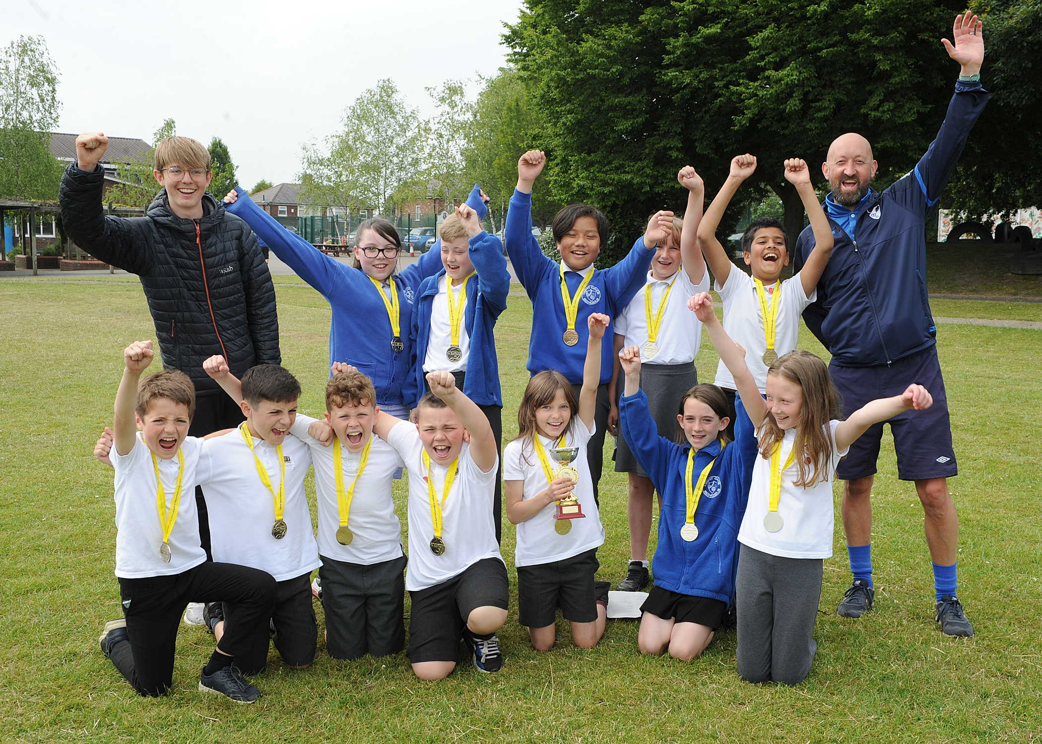 Group of children wearing medals, with two adults all cheering whilst punching the air