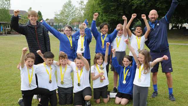 Group of children wearing medals, with two adults all cheering whilst punching the air