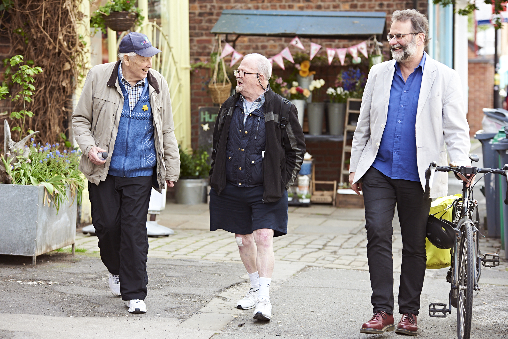 Three older adults walking and talking along a pavement, one is pushing a bike.