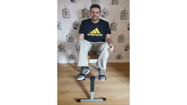 Stephen sat on a dining room chair whilst using a cycle pedal