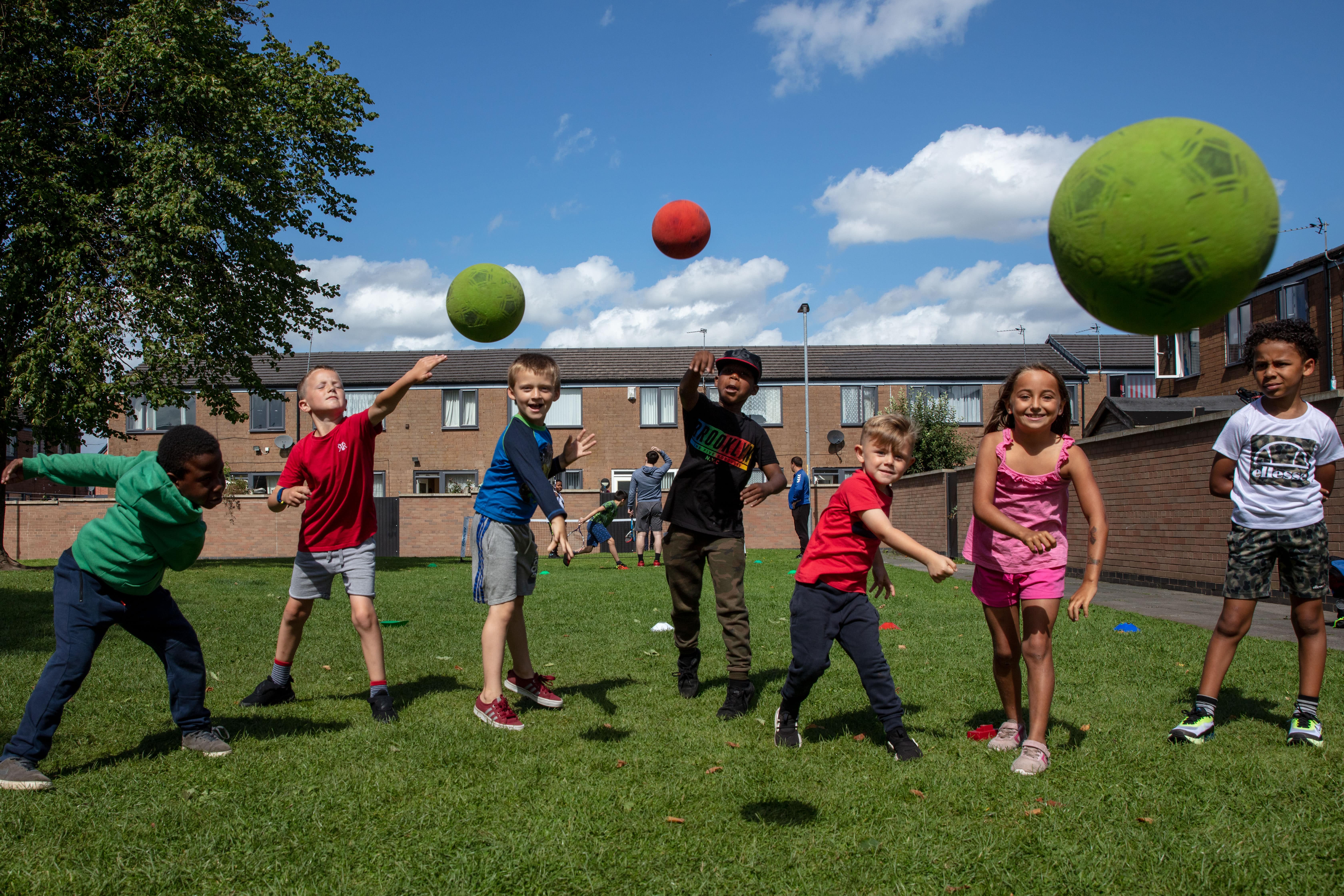 Group of young people in a residential area smiling and throwing balls in the direction of the camera
