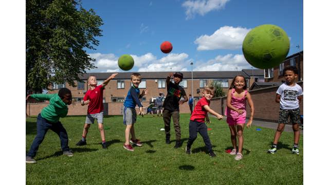 Group of young people in a residential area smiling and throwing balls in the direction of the camera