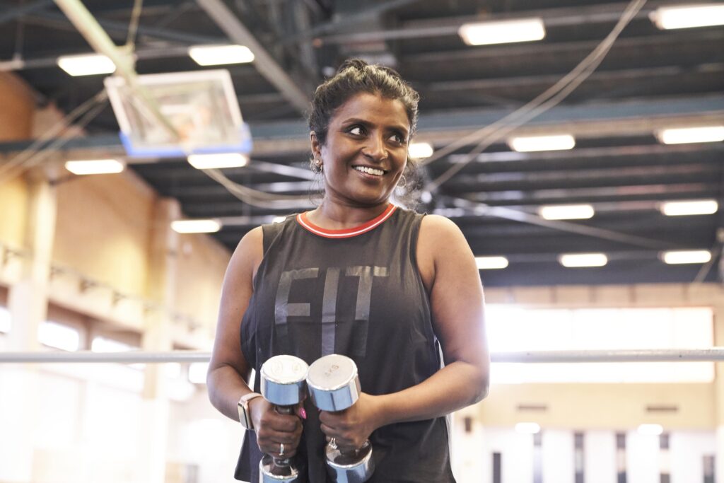 A woman uses weights in a gym while smiling