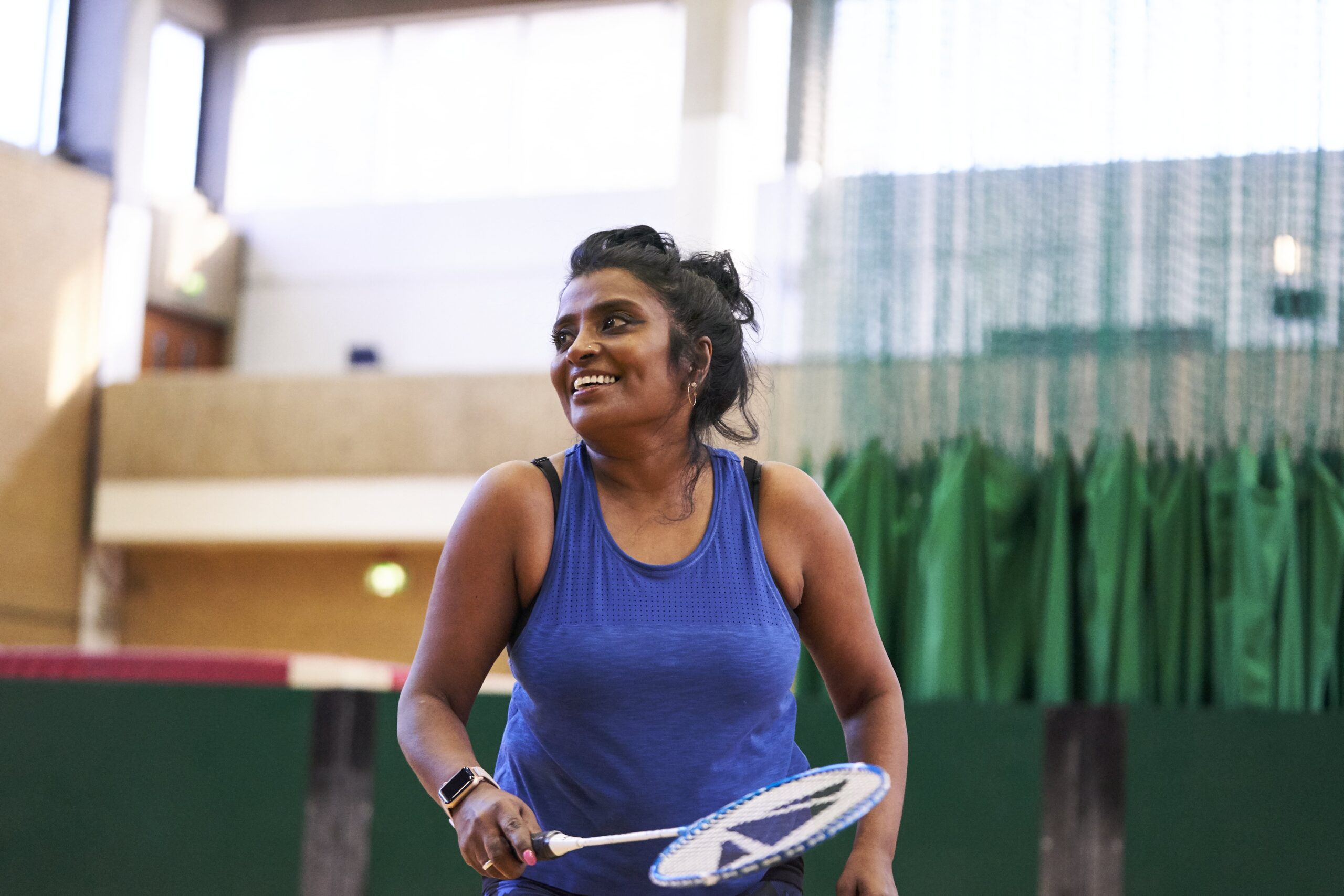 A woman smiles while playing badminton in a sports hall