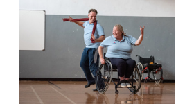 Two people dance in a leisure hall. One is using a wheelchair.
