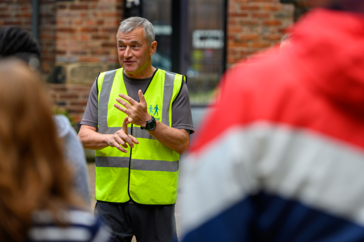 A man in a high-vis vest talks to a group, while counting on his hands.
