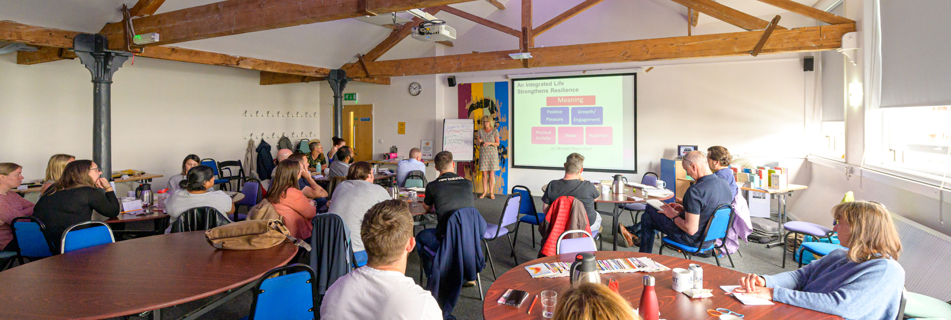 A group of people listen to a workshop while seated in a light training room with exposed beams