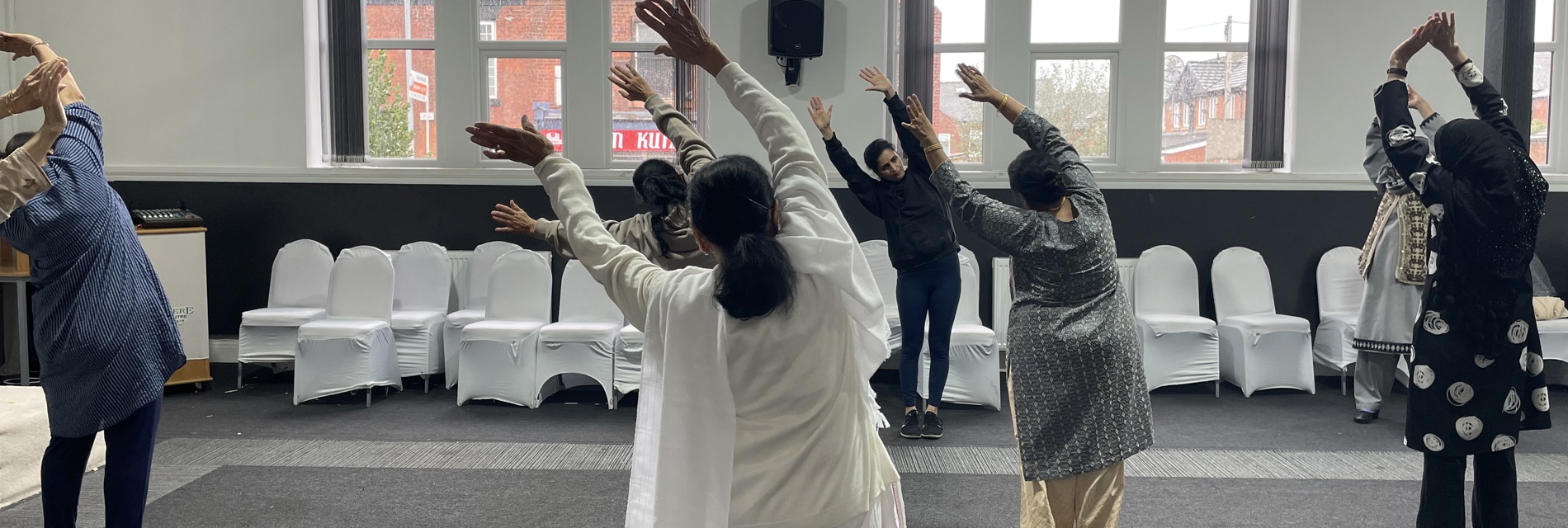 A group of women do yoga together in a light community room.