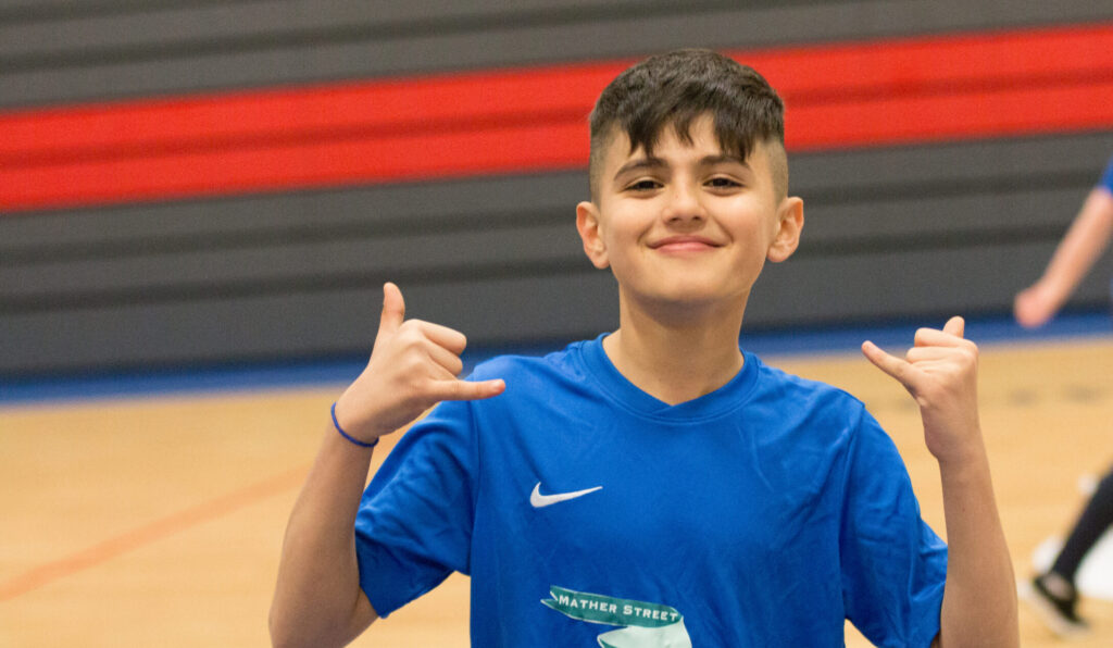 Child smiles at the camera while showing a 'shaka' hand signal