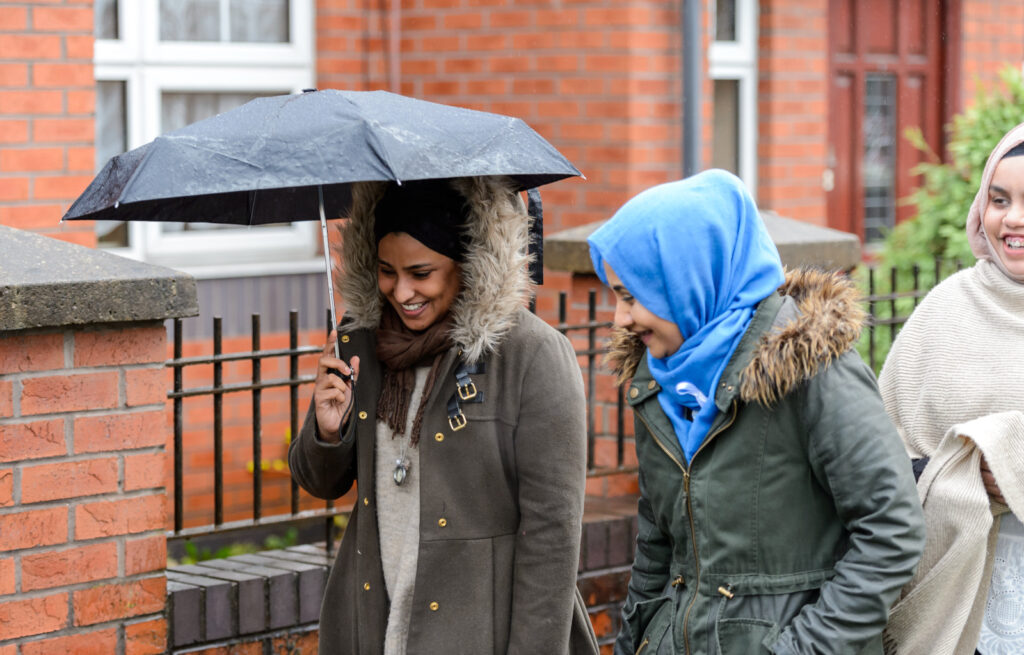 Two people in hijabs walk in the rain beneath umbrellas