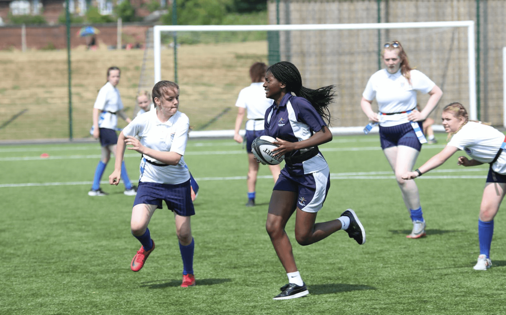 A group of young people play rugby on a sunny outdoor sports pitch