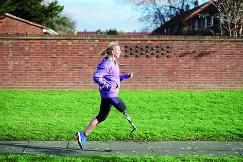 A runner with lower leg amputation and prosthetic runs along a tarmac path in a park