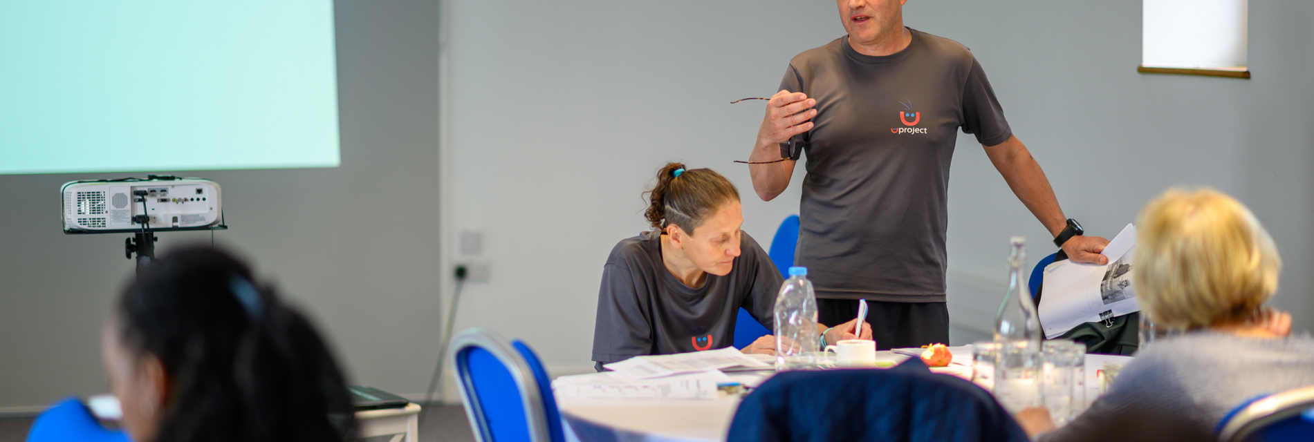 A trainer stands at the front of a training, explaining something to the room