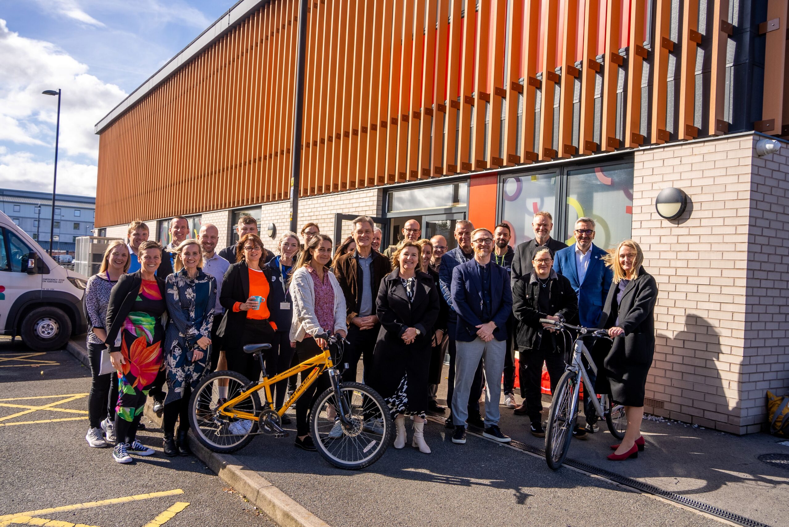 A group of people stand outside the Leigh bike library, smiling in the sunshine.