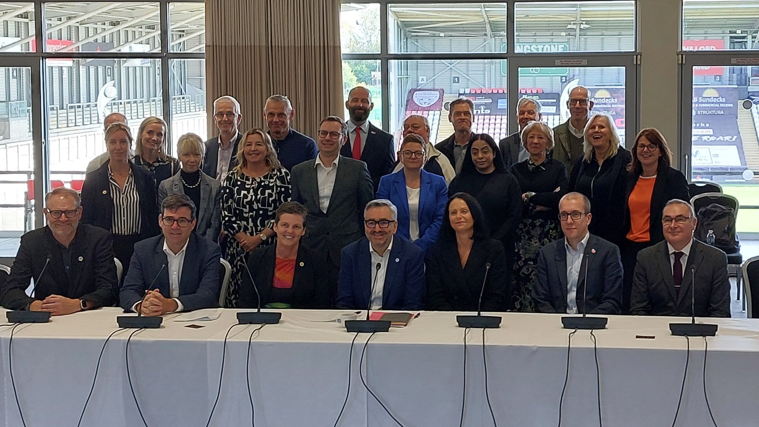 A group of community stakeholders sit and stand in front of a long table