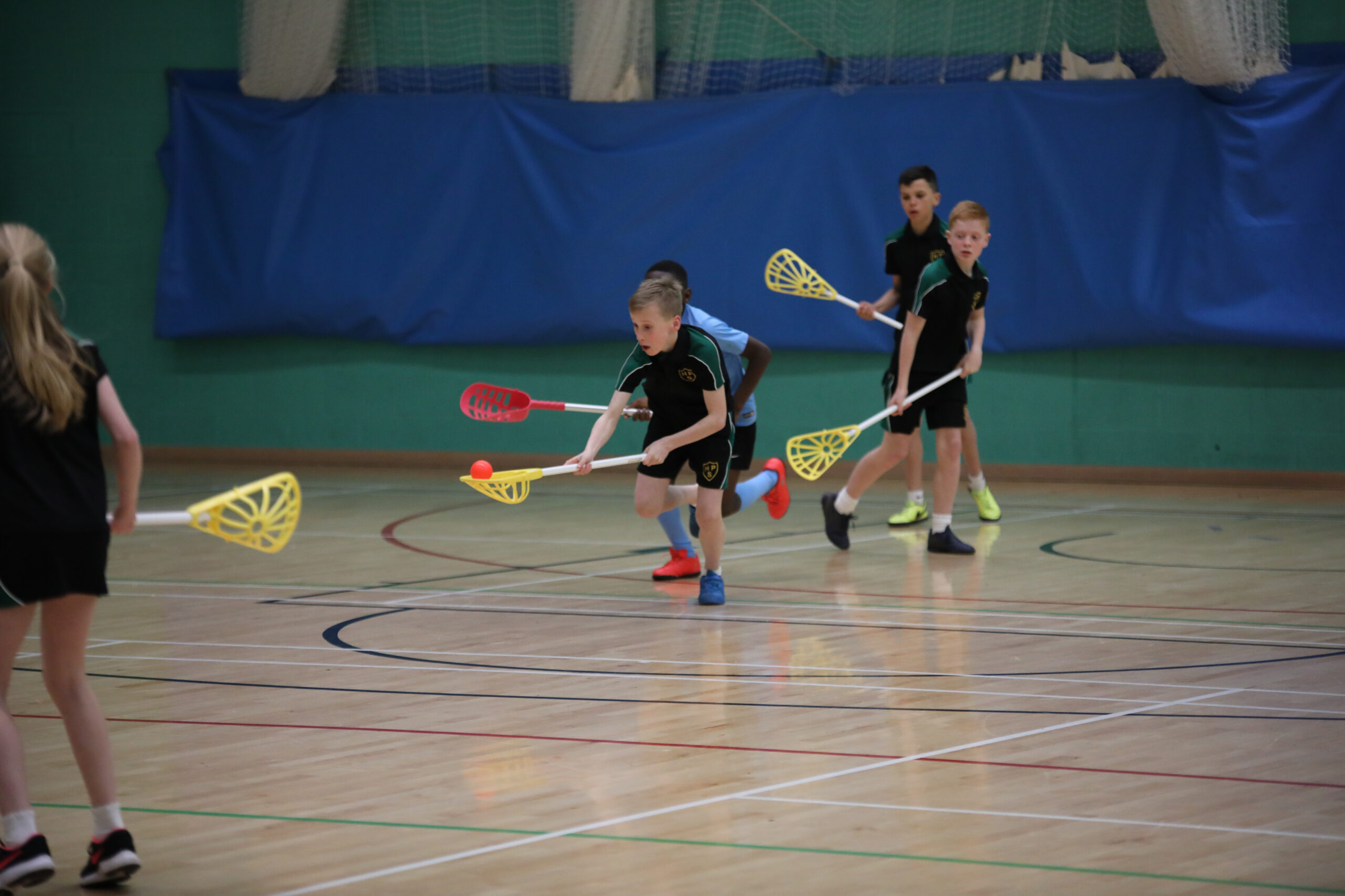 children playing lacrosse in a school sports hall