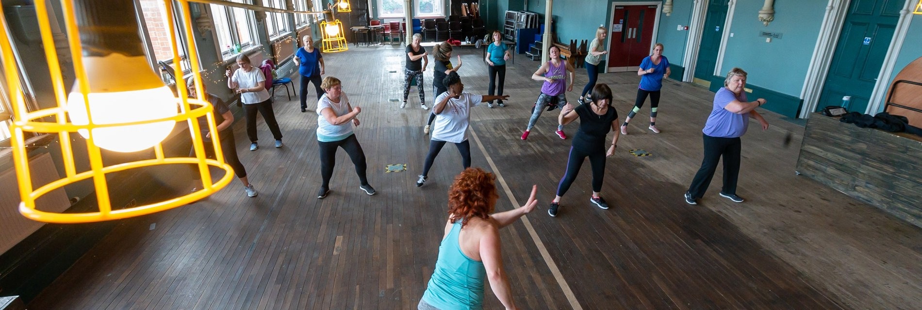 A group of adults enjoy a dance class in a Victorian community hall