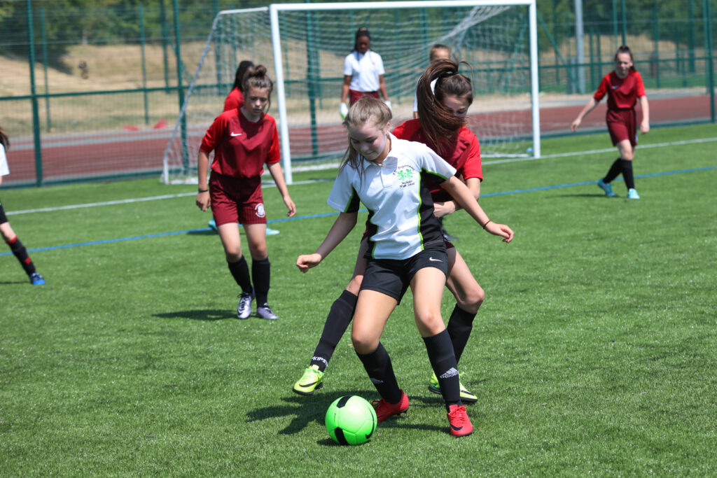 group of girls playing football on an astro turf, ball is green