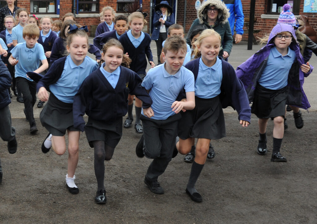 school children running in a playground, in blue and grey uniforms