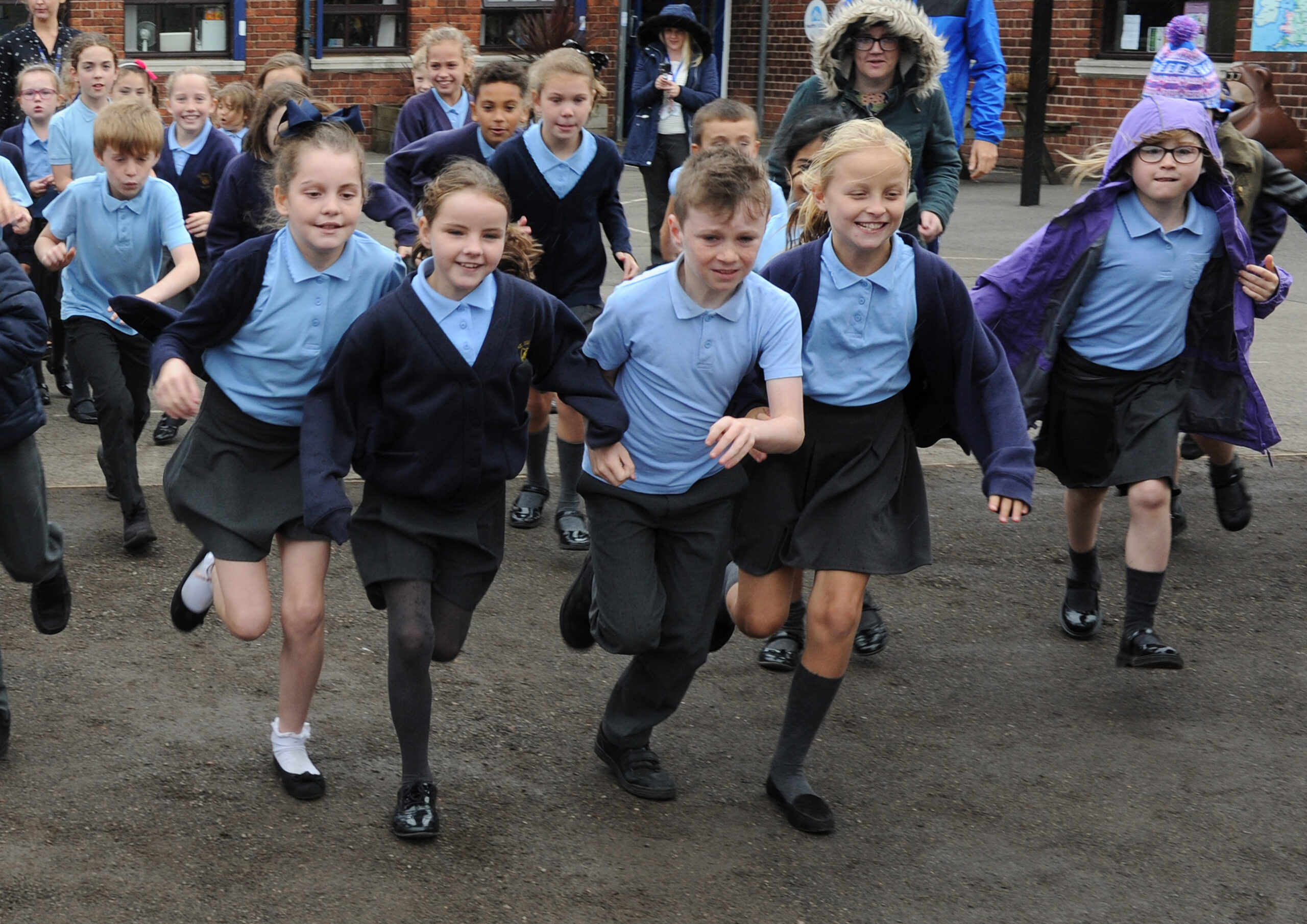 school children running in a playground, in blue and grey uniforms