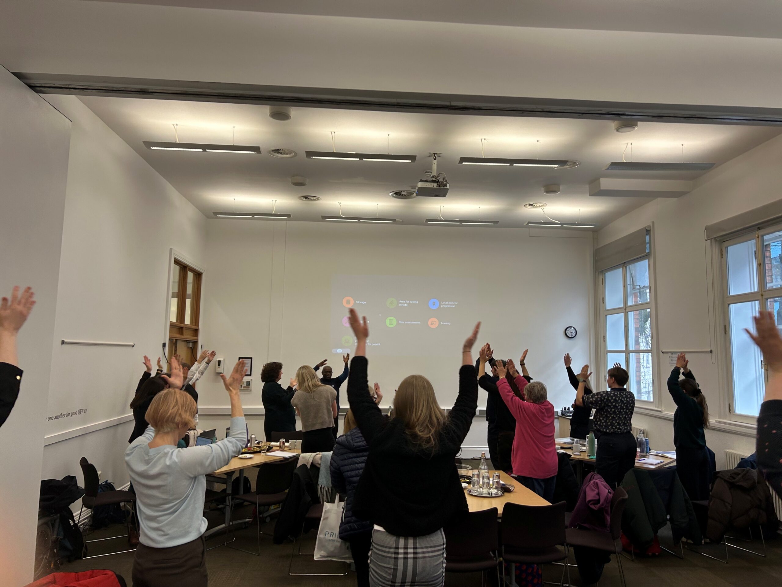 A group of seated people in a conference room raise their arms in the air.