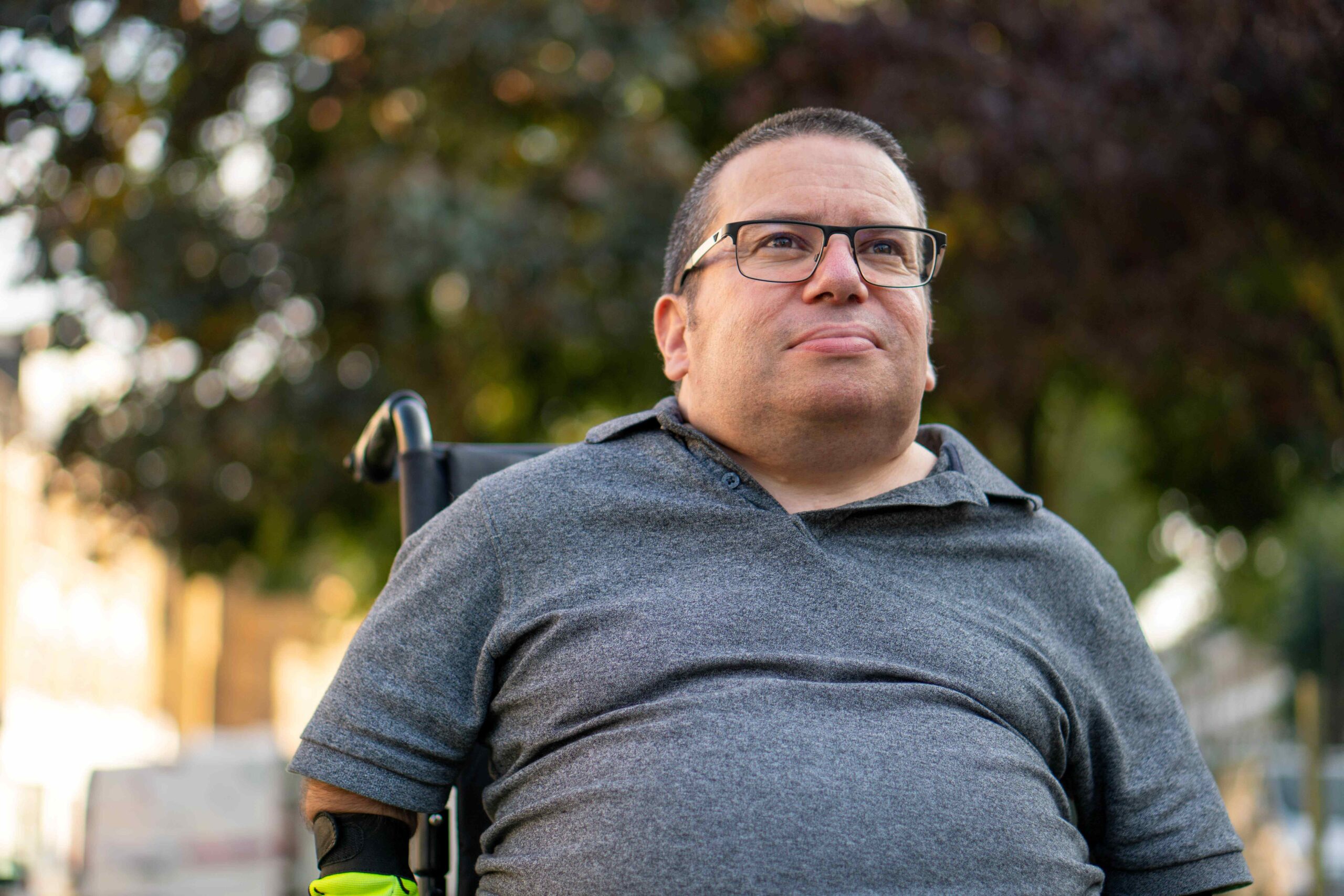 A man wearing glasses looks into the distance while seated in a wheelchair.