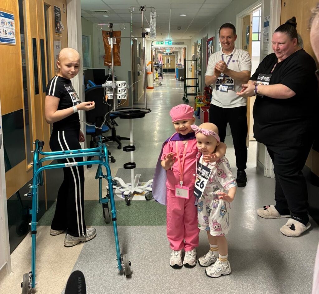 Two children complete the Mini Marathon in the hallway of a hospital ward, while staff members applaud them