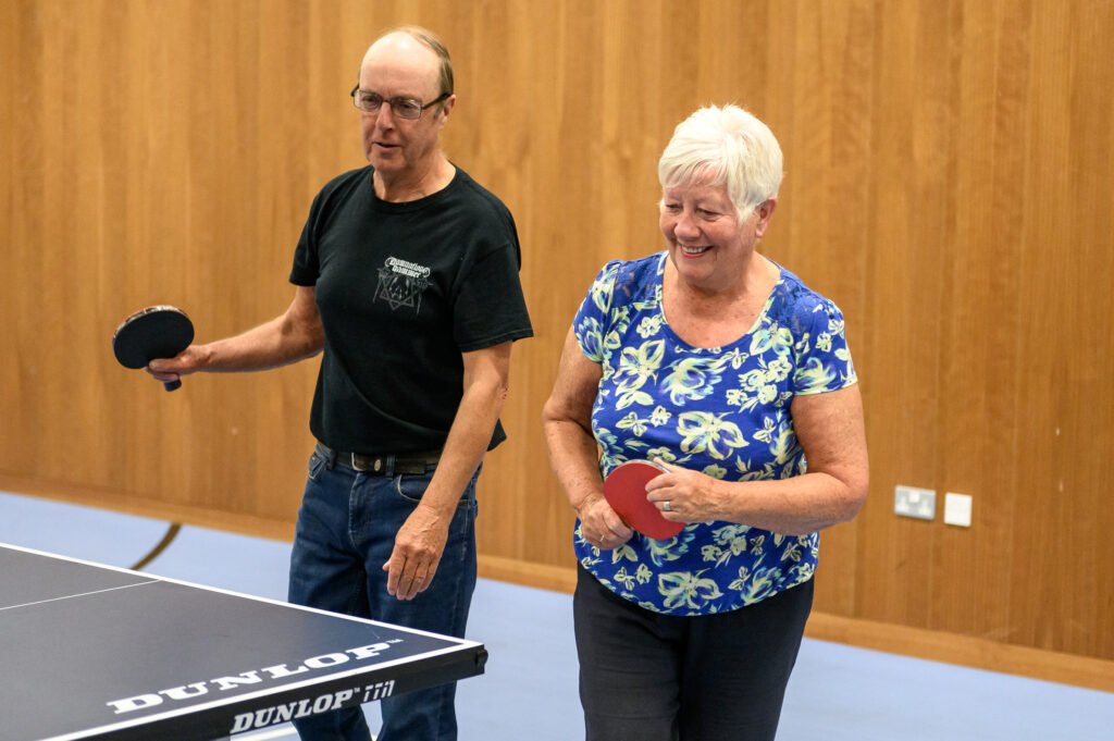 Two adults play table tennis while smiling