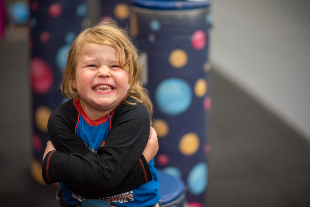 A young child smiles and hugs herself while smiling