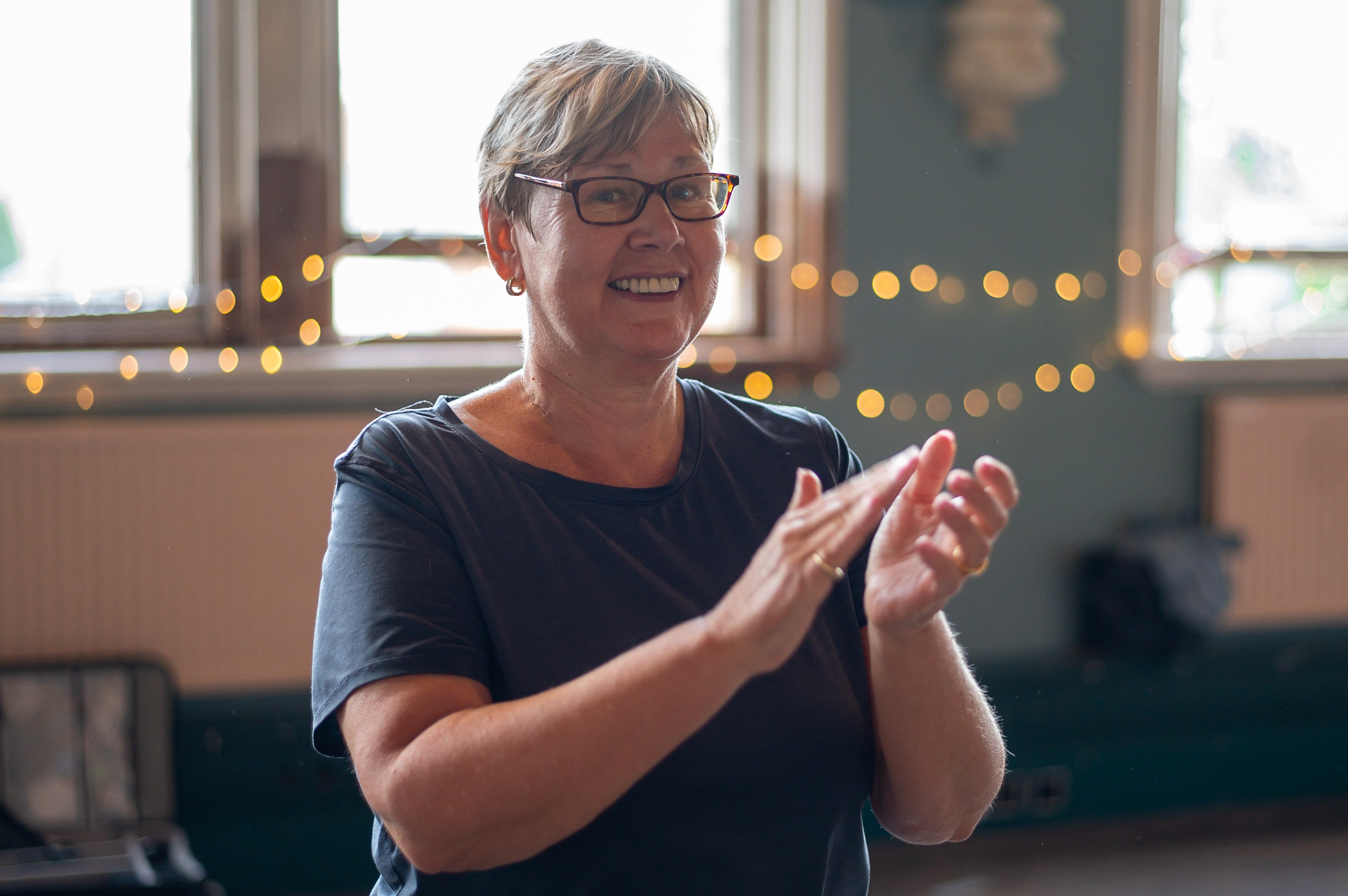 An adult dances and claps in a bright community hall
