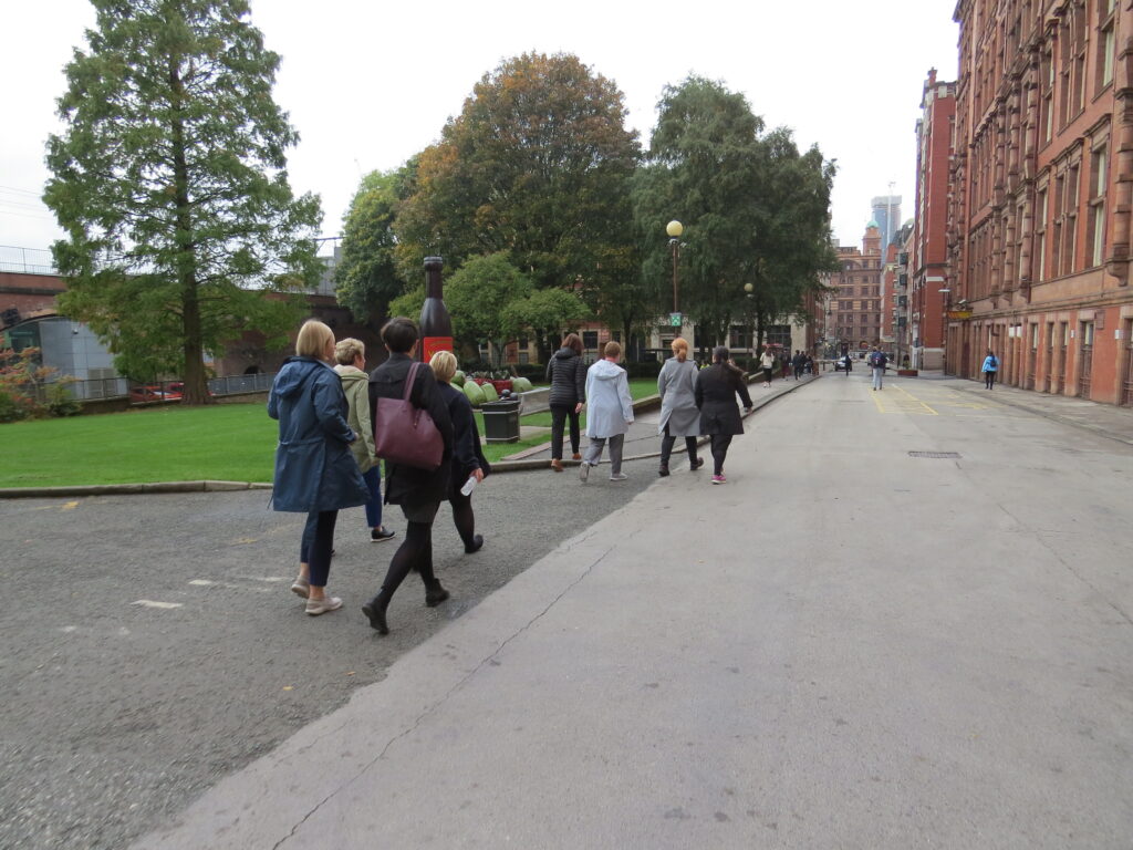 A group of adults walk along Sackville Street in Manchester on a cloudy day