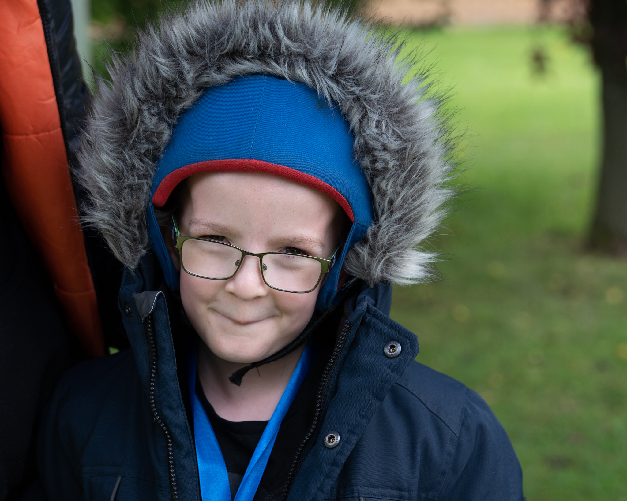 A young person outdoors in a big hood, smiling at the camera