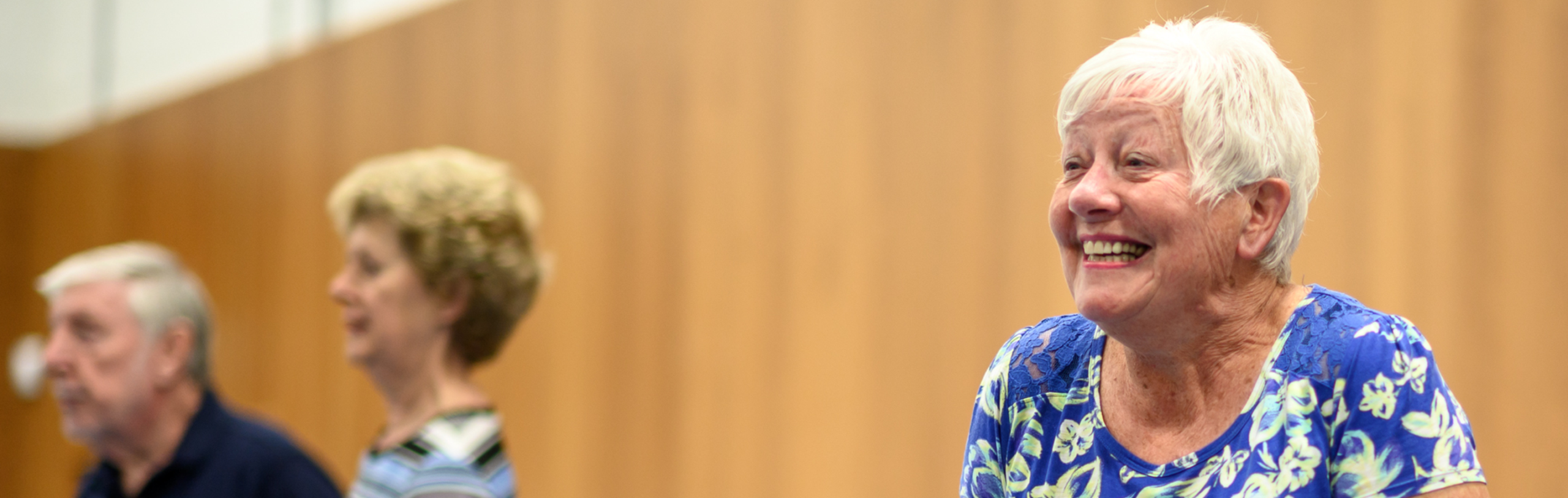 An older person wearing a blue dress, giggling indoors