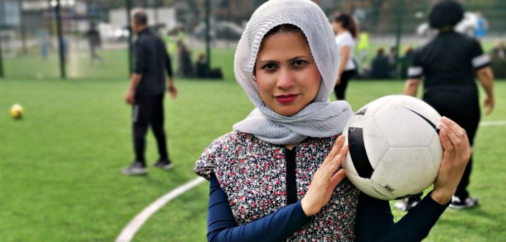 A person in a hijab holding a football and looking into camera