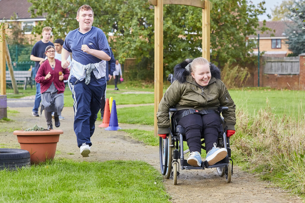 A group of smiling children run, walk and wheel along a path next to green space