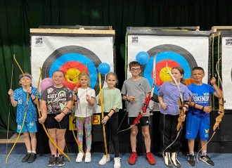 A group of children pose in front of target boards with their bows for archery practise